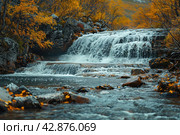 Picturesque waterfall in the forest in autumn. The water rushes forcefully over multi-level rocky rapids, creating a striking contrast with the warm colors of the autumn foliage surrounding the pond. The leaves of the trees, painted in golden and copper tones, glow against the background of dark blue water and stones, which adds peace and harmony to the scene. Стоковое AI-изображение, AI-художник Анна Кривицкая / Фотобанк Лори