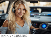 A beautiful blonde girl at an auto sound competition. Car music. Subwoofers, amplifiers, acoustics. Car audio system. Стоковое AI-изображение, AI-художник Александр Поташев / Фотобанк Лори