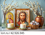 Orthodox Easter. Easter cake, painted eggs, icons, faces of saints, flowers, church candles and Easter decor on a wooden table in an old village house. Стоковое AI-изображение, AI-художник Photojuli / Фотобанк Лори