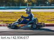 male kart racer drives quickly along the circuit of the autodrome, side view. Стоковое AI-изображение, AI-художник Александр Довянский / Фотобанк Лори