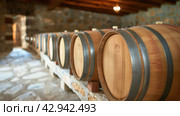 large oak barrels for maturing wine in a wine cellar in a row in perspective. Стоковое AI-изображение, AI-художник Александр Довянский / Фотобанк Лори