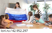 Smiling young female teacher conducting lesson for preteens, showing state flag of in audience of middle school. Стоковое видео, видеограф Яков Филимонов / Фотобанк Лори