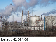 Нефтеперерабатывающий завод. Индустриальный пейзаж. Вид на промышленные сооружения и большие ёмкости для нефтепродуктов на территории НПЗ. В небе дым. Промышленность и нефтепереработка. Переработка нефти и производство топлива. Стоковое фото, фотограф Андрей Степанов / Фотобанк Лори