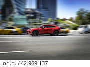 Red sports car Lamborghini Urus is driving down the street. Side view of fast moving SUV car on the city highway. Редакционное фото, фотограф Константин Григорьев / Фотобанк Лори