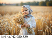 Russian Russian girl in a white dress and a Russian shawl holds golden ears of wheat against the background of a ripening field. The concept of planting and harvesting a rich harvest. Rural landscape. Стоковое AI-изображение, AI-художник Photojuli / Фотобанк Лори