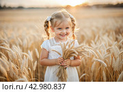 Russian Russian girl in a white dress and a Russian shawl holds golden ears of wheat against the background of a ripening field. The concept of planting and harvesting a rich harvest. Rural landscape. Стоковое AI-изображение, AI-художник Photojuli / Фотобанк Лори