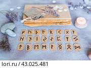 Scandinavian runes for fortune telling are  in three rows, a book, stones and a candle on the table. Стоковое фото, фотограф Елена Руй / Фотобанк Лори