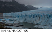 An amazing glacier stretches between the mountain slopes to the horizon. A mass of blue ice with cracks, sharp peaks, and crevices. Thawed ice floes float in a glacial lake. Cloudy. Fog. Perito Moreno. Стоковое фото, фотограф Вера Ивановна Кубарева / Фотобанк Лори