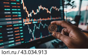 Bitcoin in a man's hand against the background of currency exchange rate charts on a laptop monitor screen. Стоковое AI-изображение, AI-художник Ярославский Максим / Фотобанк Лори