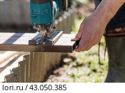 A man holds a battery-powered electric saw and builds new beds in a greenhouse made of wood-polymer composite. Macro photography. Side view. Preparing for the spring garden season. Стоковое фото, фотограф Photojuli / Фотобанк Лори