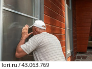 An elderly man with gray hair in a baseball cap peeps through the window of someone else's house. Стоковое фото, фотограф Светлана Акифьева / Фотобанк Лори
