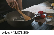 There is a wok on the stove with onions in it, and vegetables are scattered around the table for cooking. Стоковое видео, видеограф Strunov David / Фотобанк Лори