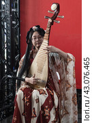 St. Petersburg, Russia-February 3, 2024: A young Chinese woman in a traditional costume plays a Chinese musical instrument called pipa. Редакционное фото, фотограф Регина Ерофеева / Фотобанк Лори
