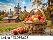 The concept of the Russian Orthodox holiday yablochny spas. A beautiful wicker basket made of vines with red ripe apples on the background of an Orthodox church. Стоковое AI-изображение, AI-художник Photojuli / Фотобанк Лори