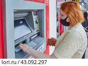 Young white woman wearing PPE gets cash in form of paper currency at street ATM. (2021 год). Редакционное фото, фотограф Владимир Григорьев / Фотобанк Лори