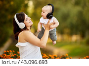 Smiling woman with child in cordless headphones sit in park. Стоковое фото, фотограф Владимир Григорьев / Фотобанк Лори