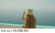 A woman in a hat views the endless sea from a high coastal vantage point, embodying tranquility. Ocean horizon meets the clear sky. Стоковое видео, видеограф Igor Tichonow / Фотобанк Лори