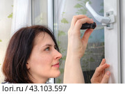 Repair of handle on double hung vinyl window with mosquito net. Young European woman fixing lock with screwdriver. Стоковое фото, фотограф Владимир Григорьев / Фотобанк Лори
