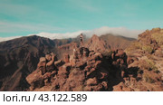 A person perches on a cliff edge with a panoramic view of mountainous terrain. Woman surveys the sprawling wilds, the peaks rising over cloudy sky. Стоковое видео, видеограф Ольга Сухарева / Фотобанк Лори