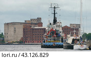 Kaliningrad, Russia - June 20, 2022: Industrial part of the city. Bank of Pregol River. Different ships. Tug boat in seaport on the Pregolya River. Редакционное фото, фотограф YuryKara / Фотобанк Лори