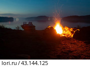 Карелия. Лахденпохский район. Пейзаж с моторной лодкой и костром вечером в походе на островах (2020 год). Редакционное фото, фотограф Сергей Крамарев / Фотобанк Лори