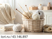 Balls of yarn in a wicker basket in white and beige tones. Needlework, textiles, knitting. Winter season, small business, handmade clothes. Стоковое AI-изображение, AI-художник Photojuli / Фотобанк Лори