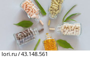 Video of glass vials with capsules of food bio additives and green plants on light background. Five types of natural dietary supplements with herbals and omegas. Flat lay, close-up, top view. Стоковое видео, видеограф Виктория Катьянова / Фотобанк Лори