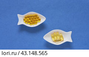 Dietary supplements or nutrition additions with fish oil, vitamin E and omega acids. Concept of preventing heart disease using fish oil. Flat lay of gelatin capsules on fish-shaped plates on blue background. Стоковое видео, видеограф Виктория Катьянова / Фотобанк Лори
