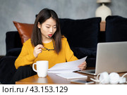 Asian woman working at home looking at documents. Beautiful Japanese female freelancer. Стоковое фото, фотограф Natalia Gdovskaia / Фотобанк Лори