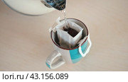 Drip bag fresh coffee. Pouring hot water into blue cup with drip coffee bag. Instant freshly brewed cup of ground coffee. Coffee Trend. Quick way to brew using paper filter. The process of brewing. Стоковое видео, видеограф Марина Демидюк / Фотобанк Лори