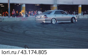 A large silver drift car burns rubber for the amusement of the audience with smoke at the demonstration performances at the Mega Belaya Dacha site. Slow motion. Russia. Moscow. 19.05.2024. Стоковое видео, видеограф Ярославский Максим / Фотобанк Лори