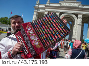 Мужчина играет на гармони у арки Центрального входа на ВДНХ в городе Москве, Россия (2024 год). Редакционное фото, фотограф Николай Винокуров / Фотобанк Лори