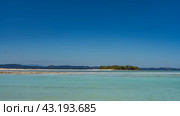 A tropical island covered with green vegetation and a sandbar are visible in the aquamarine ocean. Tiny silhouettes of people on a sandy beach. Mountains on the horizon. Clear blue sky. Copy space. Стоковое фото, фотограф Вера Ивановна Кубарева / Фотобанк Лори