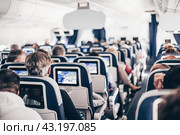 Interior of airplane with passengers on seats and stewardess in uniform walking the aisle, serving people. Commercial economy flight service concept. Стоковое фото, фотограф Matej Kastelic / Фотобанк Лори