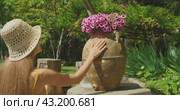 A woman touches a flower pot on a pedestal surrounded by green plants in the garden. Tourist has immersive contact with antique vase. Стоковое видео, видеограф Ольга Сухарева / Фотобанк Лори