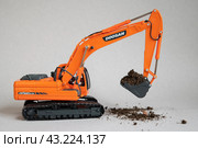 Экскаватор Doosan южнокорейского производства. Специальный транспорт для копания земли. Мини-экскаватор – игрушечная миниатюрная модель с землей в ковше. (2023 год). Редакционное фото, фотограф Дорощенко Элла / Фотобанк Лори