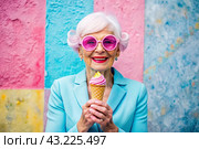 Portrait of an extraordinary, stylish, fashionable elderly woman, a pensioner of 70 years old, with glasses and ice cream in her hand. The concept of happy seniors and delicious desserts. Стоковое AI-изображение, AI-художник Photojuli / Фотобанк Лори