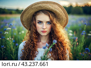 Spring flowering. Portrait of a beautiful curly-haired girl in a straw hat in a blooming field. The girl poses and looks at the camera. Стоковое AI-изображение, AI-художник Photojuli / Фотобанк Лори
