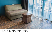 A seating area in the living room. There is a soft sofa and a coffee table in the corner on the laminate floor. Through the translucent curtains, you can see a terrace with a lattice railing, chairs. Стоковое фото, фотограф Вера Ивановна Кубарева / Фотобанк Лори