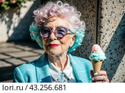 Portrait of an extraordinary, stylish, fashionable elderly woman, a pensioner of 70 years old, with ice cream in her hands on a city street. The concept of happy seniors and delicious desserts. Стоковое AI-изображение, AI-художник Photojuli / Фотобанк Лори