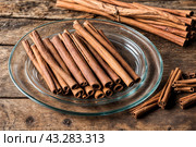 Ceylon cinnamon sticks in glass plate on wooden board, rustic style. Still life natural food of sri lankan cinnamon sticks on table at grey wall. Delicious tasty healthy concept. Copy ad text space. Стоковое AI-изображение, AI-художник Aleksandr Golubev / Фотобанк Лори