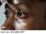 Young woman applying serum on her face. African 20s girl holding dropper and skin care product. Female applies essential oil with oily pipette. Advertising facial care cosmetics. Health, youth. Serums. Стоковое AI-изображение, AI-художник Марина Демидюк / Фотобанк Лори