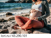 Relaxation, peace of mind, sea air. Close-up of the tummy. A pregnant woman on the beach by the sea. The concept of pregnancy, childbirth and parental responsibilities. Стоковое AI-изображение, AI-художник Photojuli / Фотобанк Лори
