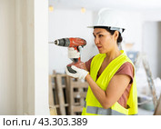 Woman builder using drill to bore hole in wall. Стоковое фото, фотограф Яков Филимонов / Фотобанк Лори