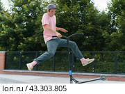 Moscow, Russia - July 1, 2020: Push scooter stunt on the urban sport ground in summer day. Boy shows  trick. Jumping. Healthy lifestyle. Extreme sports is popular among youth. Front view. Редакционное фото, фотограф YuryKara / Фотобанк Лори