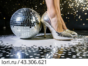 Women's legs in luxurious shiny pumps with heels at a party or disco on the background of a silver mirrored disco ball. The queen of the dance floor. Стоковое AI-изображение, AI-художник Photojuli / Фотобанк Лори