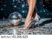 Women's legs in luxurious shiny pumps with heels at a party or disco on the background of a silver mirrored disco ball. The queen of the dance floor. Стоковое AI-изображение, AI-художник Photojuli / Фотобанк Лори