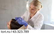 Professional elderly female trichologist performing PRP therapy to young woman, injecting platelet rich blood plasma into patient scalp to restore hair health. Стоковое видео, видеограф Яков Филимонов / Фотобанк Лори