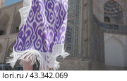 A young woman with long hair in an oriental robe and skullcap stands in the wind near an ancient mosque. Стоковое видео, видеограф Aleksey Kidisyuk / Фотобанк Лори