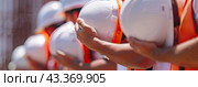 Workers in bright protective vests stand in a row and hold helmets in their hands. Стоковое AI-изображение, AI-художник Ярославский Максим / Фотобанк Лори